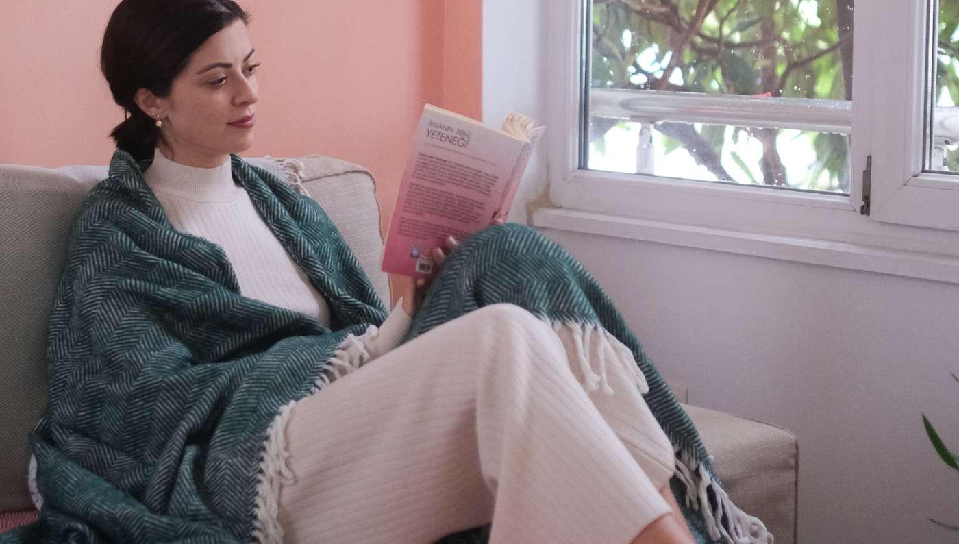 A girl wrapped in a Trimita blanket is reading a book in bed.