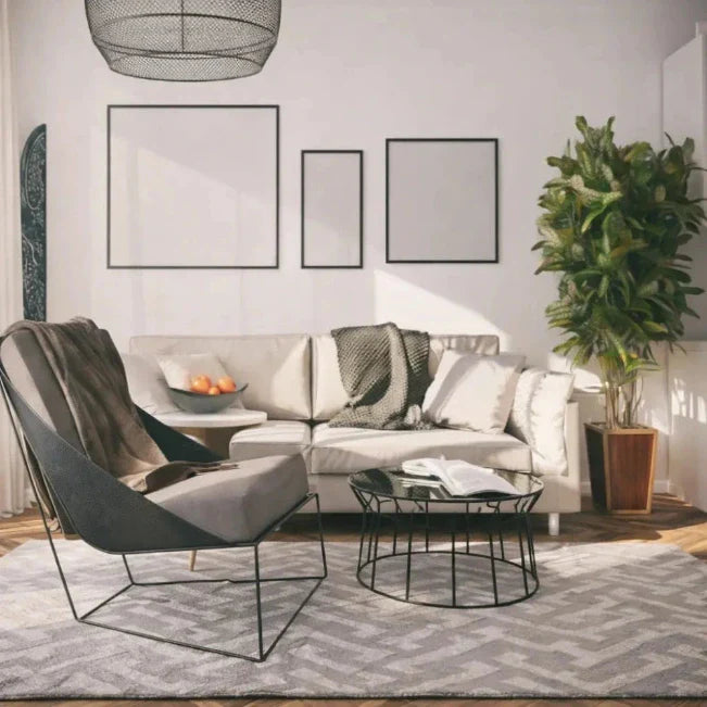 Woonkamer met een lichte bank, grijze fauteuil, ronde salontafel en een potplant.