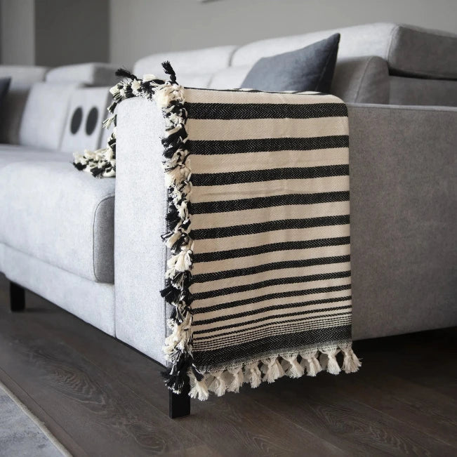 Zwart-crème gestreepte plaid met franjes over de armleuning van een grijze bank.