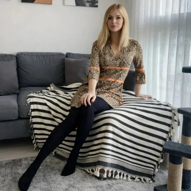 Vrouw op een grijze bank met een zwart-wit gestreepte plaid met franjes.