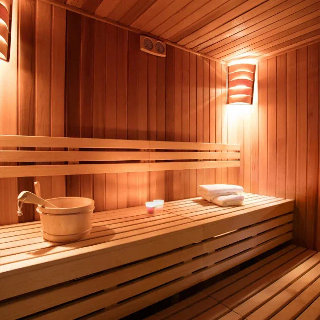 Sauna met houten wanden, banken op verschillende hoogtes, een houten emmer en warm wandlicht.