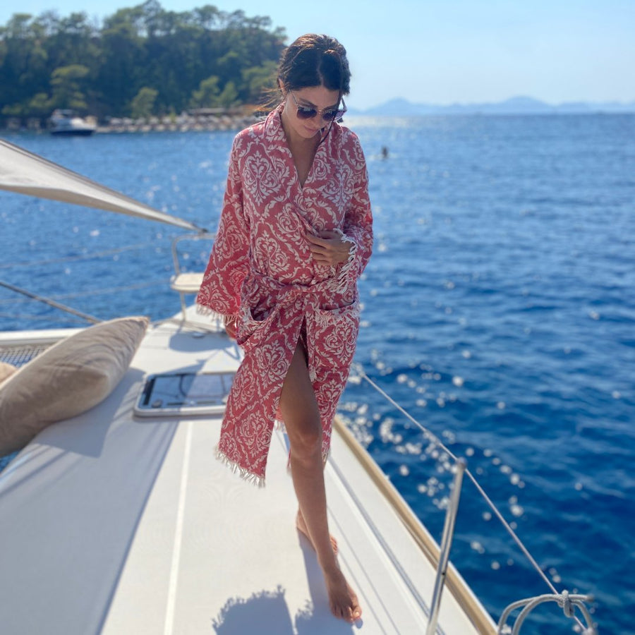 Femme portant un peignoir à motifs rouges et blancs sur le pont d’un bateau en mer.