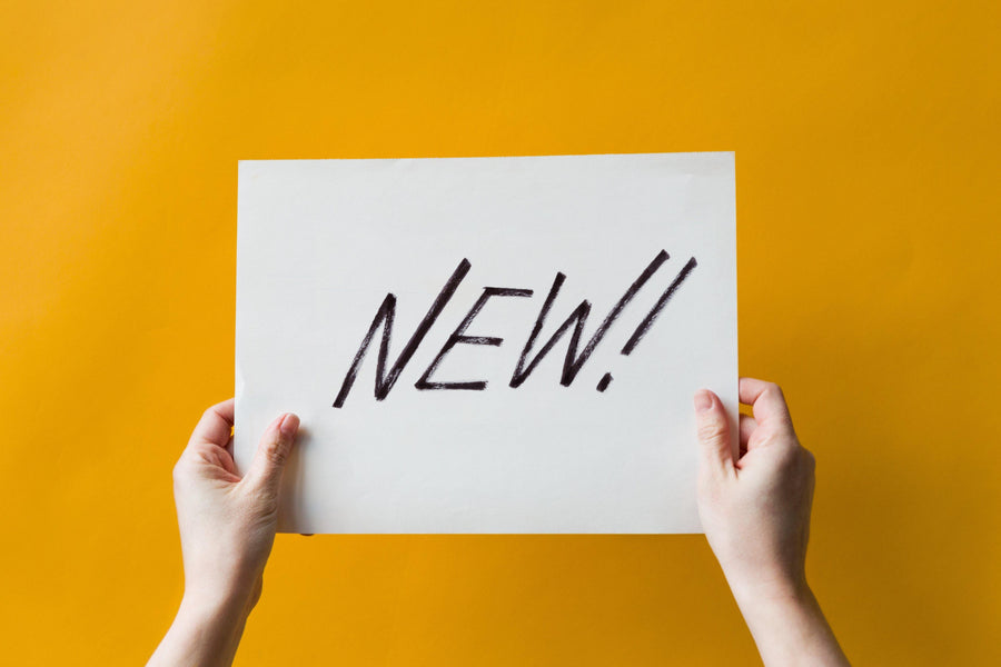 Deux mains tiennent une carte blanche portant le mot « NEW! » sur un fond jaune.