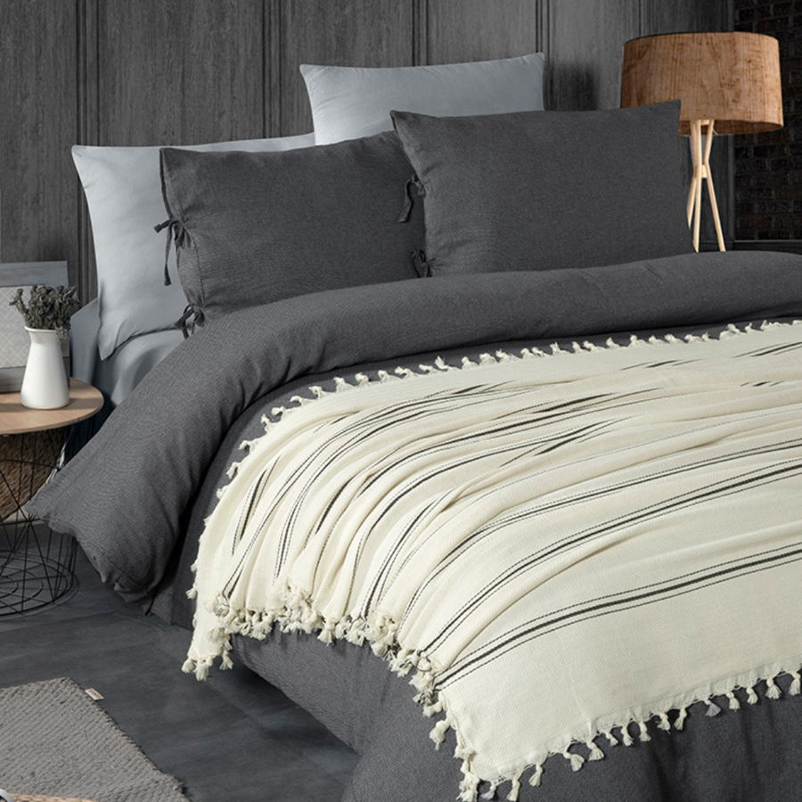 Couvre-lit crème à fines rayures foncées et franges sur un lit habillé de linge gris foncé.