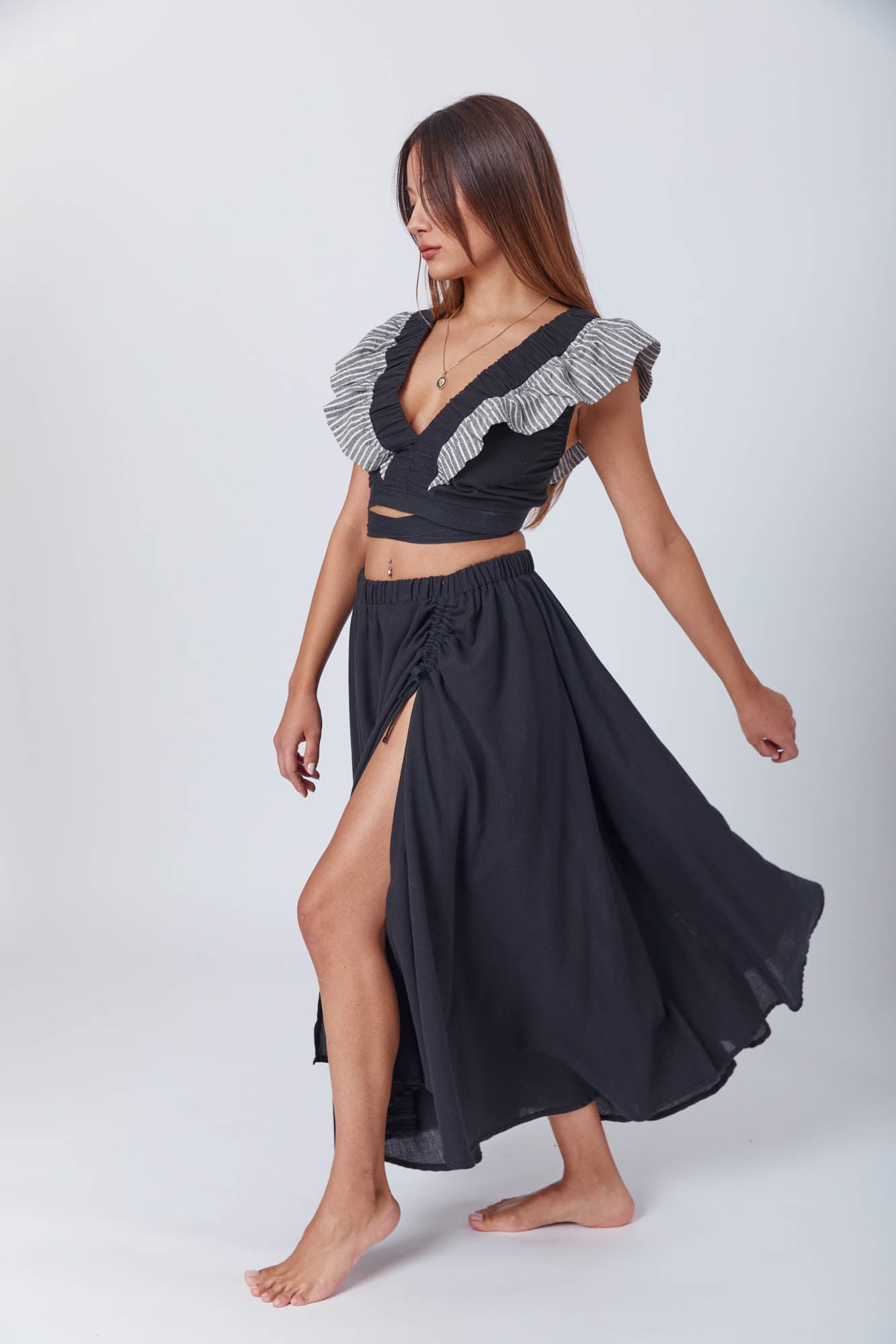 Chic, barefoot model in a black two-piece set with statement sleeves and a flowy slit skirt, exuding quiet sophistication