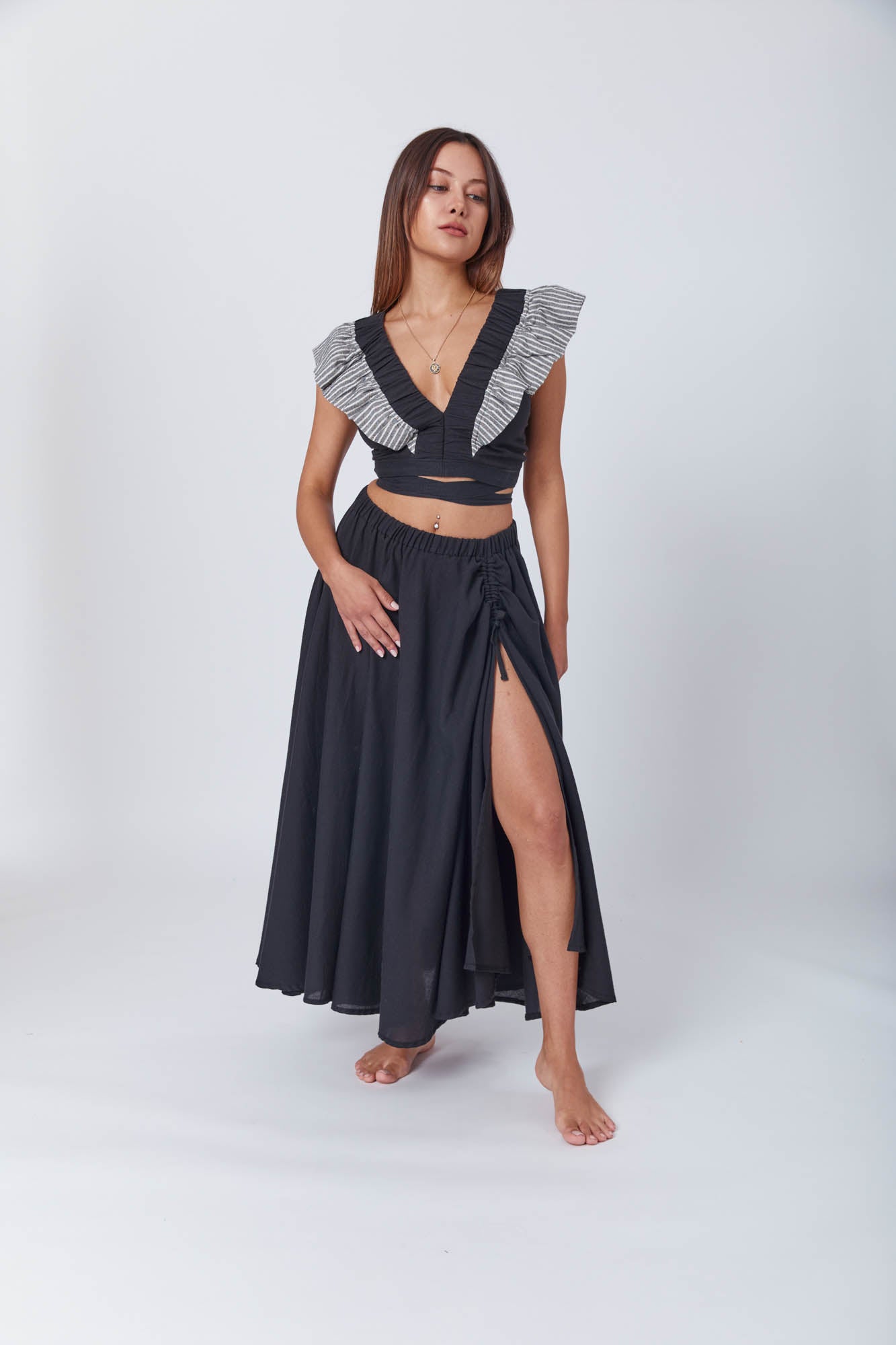 Model wearing a dramatic black outfit featuring a plunging V-neck top with layered ruffle trim and a gathered slit midi skirt