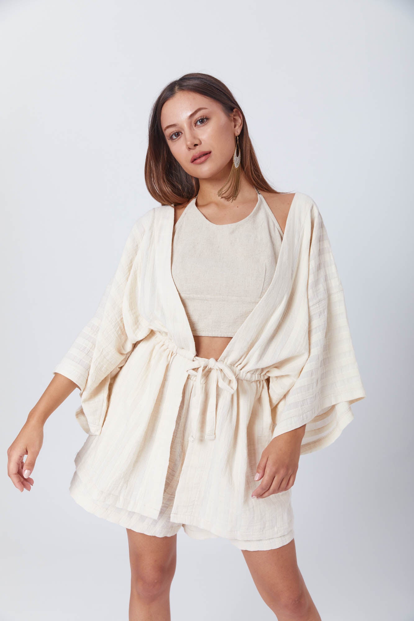 Model poses in a light, textured linen outfit featuring a halter crop top, relaxed cardigan, and high-waisted shorts, perfect for summer