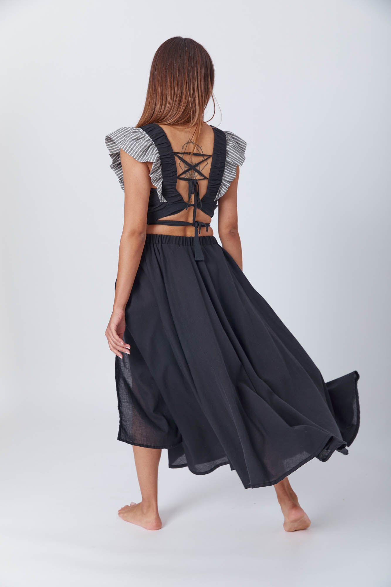 A woman poses in a black wrap crop top with ruffled striped sleeves and a matching high-waisted black skirt with a side slit