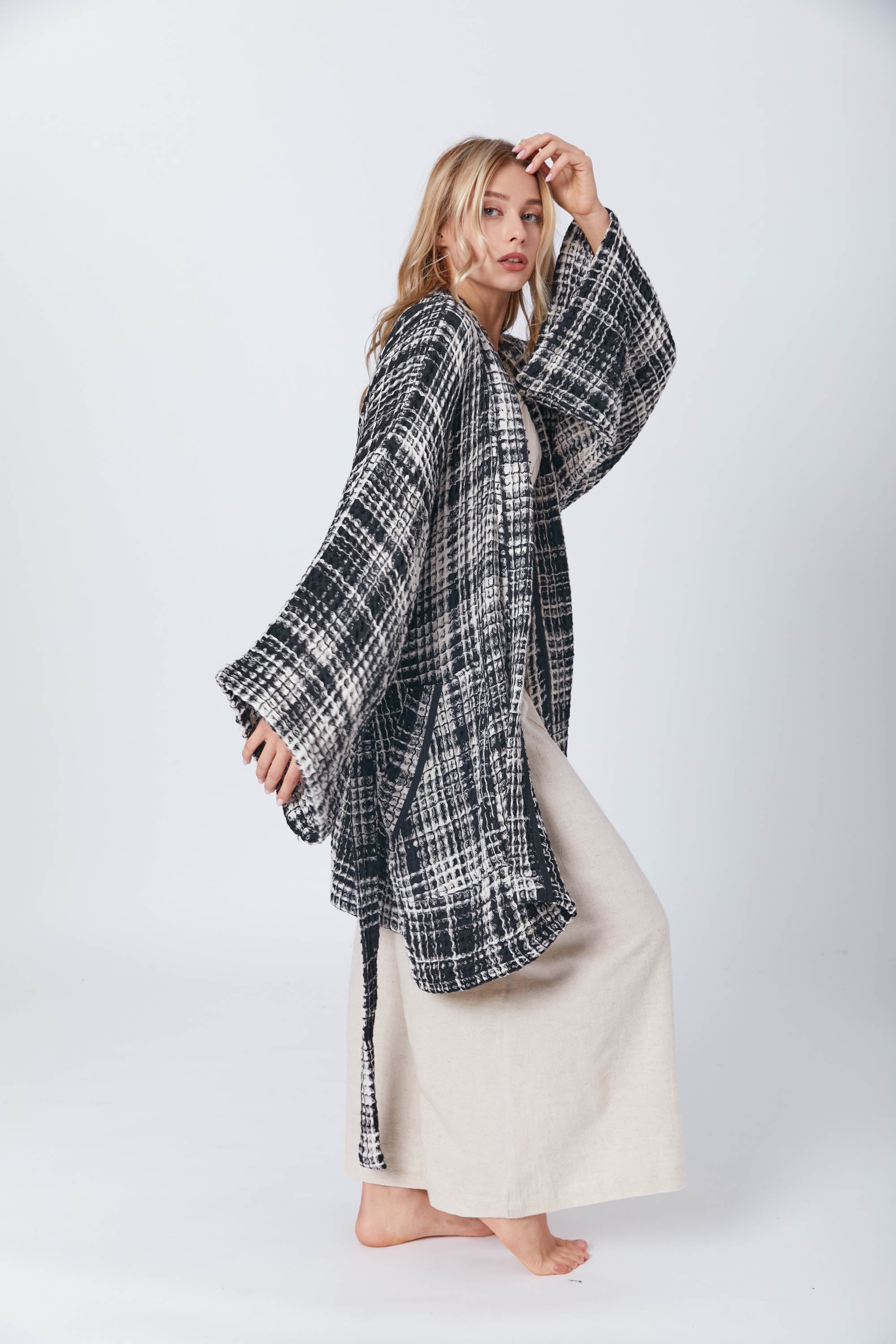 Blonde woman in a motion-filled pose, showcasing a soft neutral-toned ensemble contrasted by a bold checkered outer layer