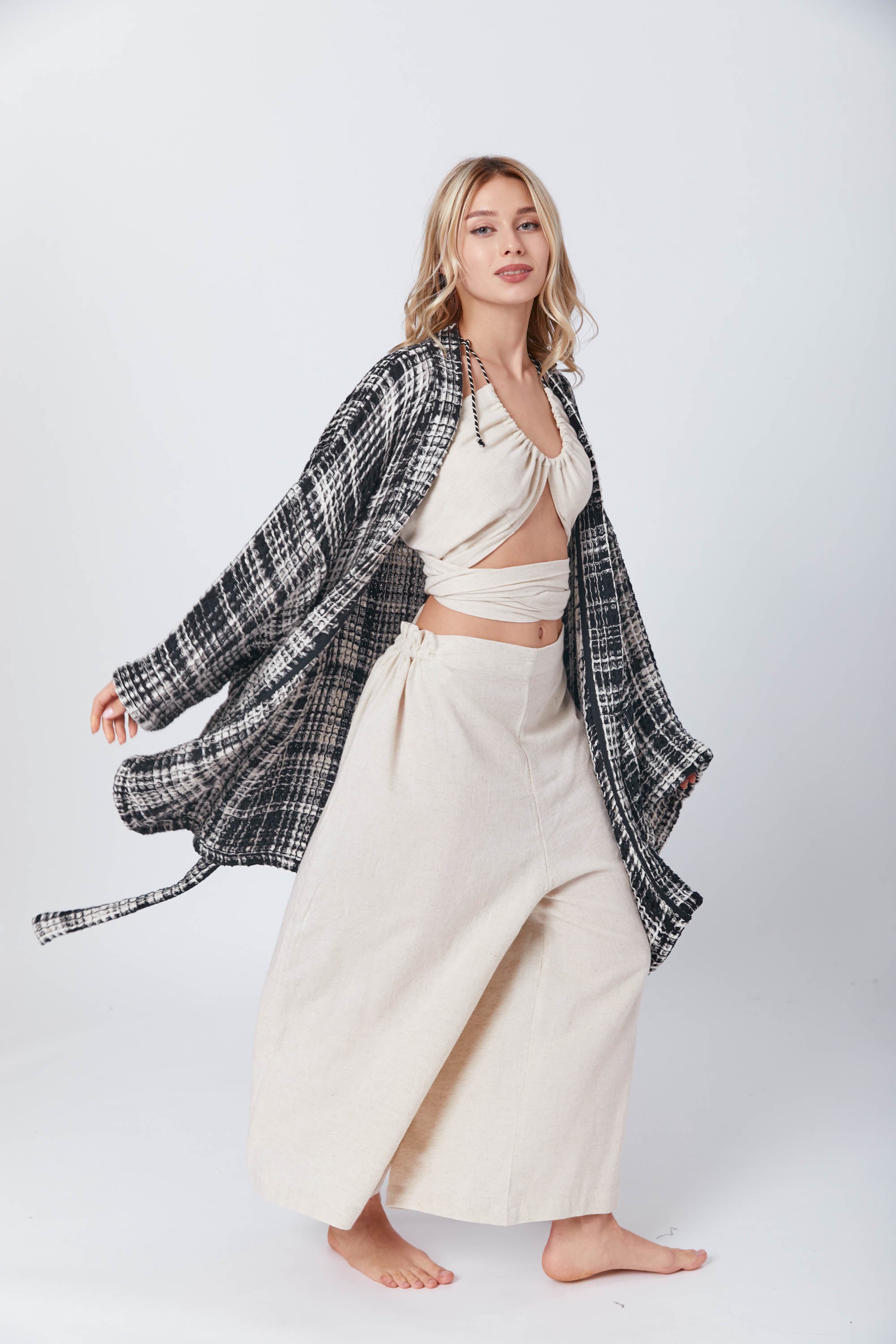 A woman poses in a light cream halter wrap top and wide-leg pants, layered with a black and white checkered robe-style jacket-Trimita.