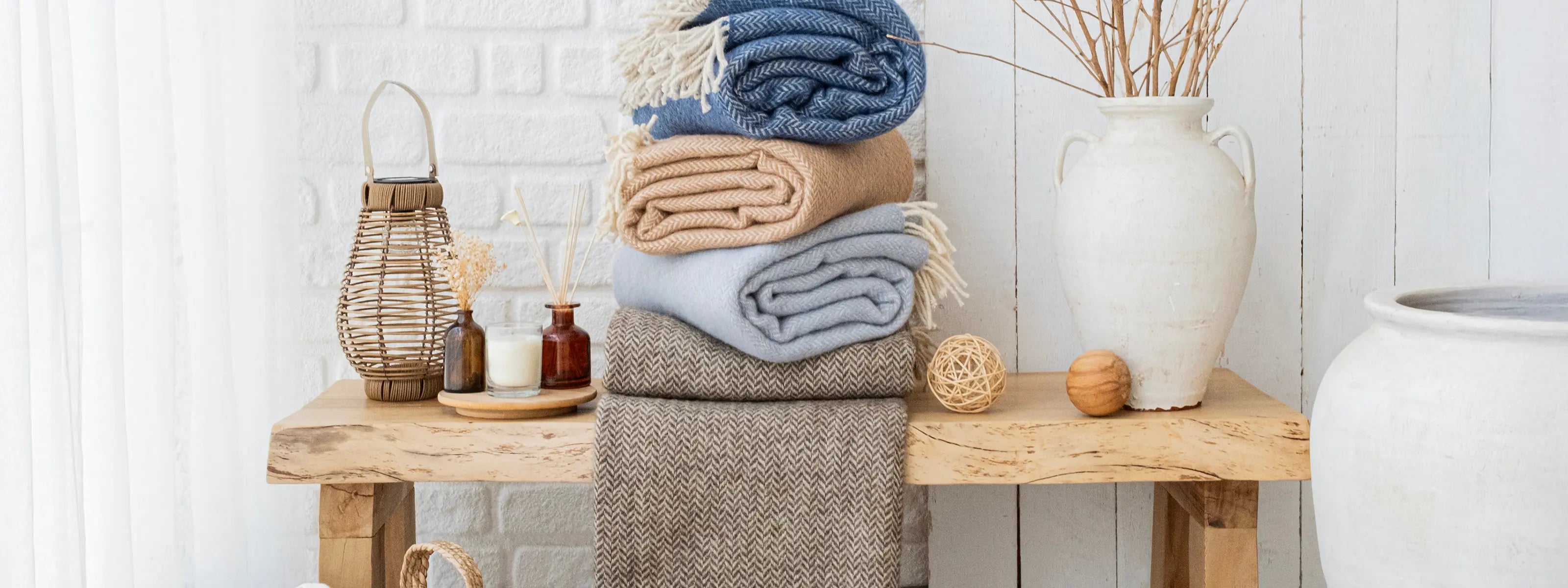 Trimita sustainable cotton and wool blankets neatly stacked on a rustic wooden table with minimalist décor — handcrafted eco-friendly textiles from Türkiye for natural home comfort.”