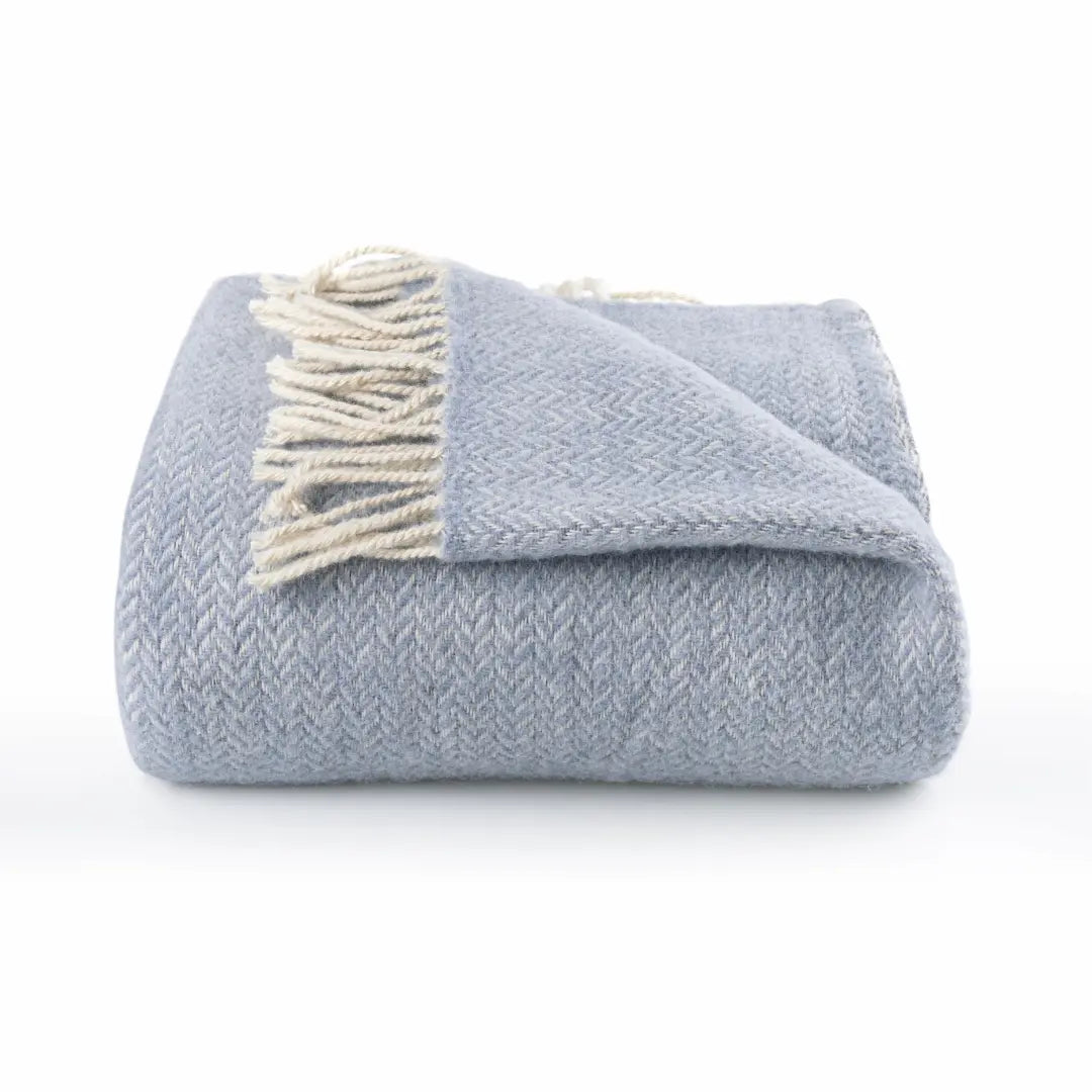 Folded light blue blanket with white fringe on a white background