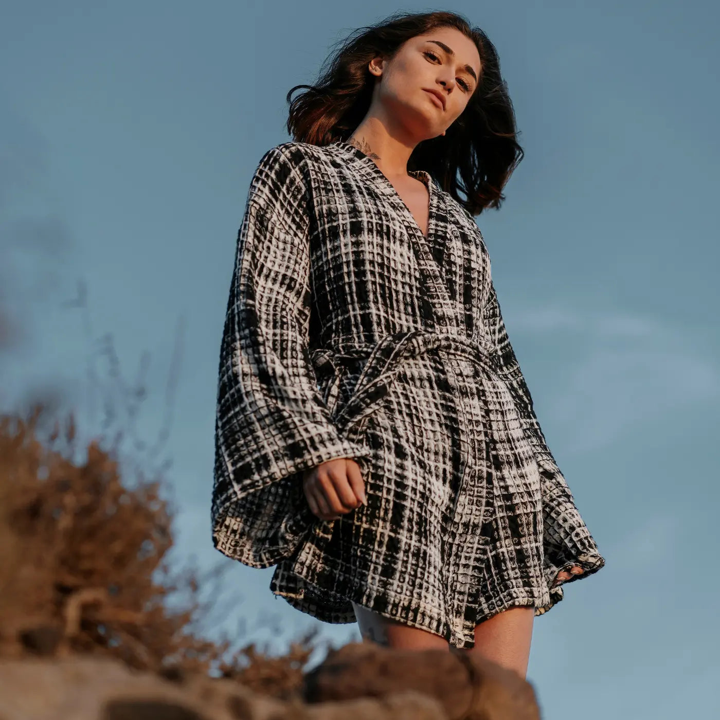 Eleganter Damen-Bademantel in Schwarz-Weiß Tweed-Optik mit Gürtel vor blauem Himmel. Kostenloser Versand bei Bestellungen über 50€.