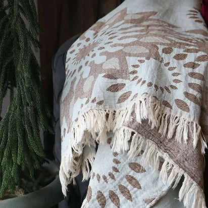 A close-up photograph highlighting the woven texture and intricate brown sunflower pattern on a light blue Turkish towel (Pestemal), with white knotted fringes at the bottom.