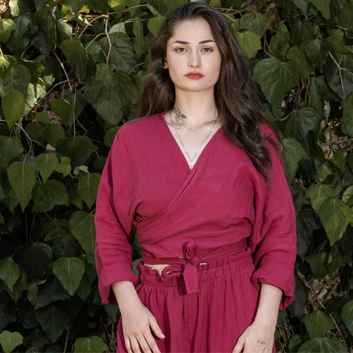 Close-up portrait of a woman wearing a magenta double-cloth muslin crossover wrap crop top, showcasing the V-neck design and organic crinkled fabric texture.