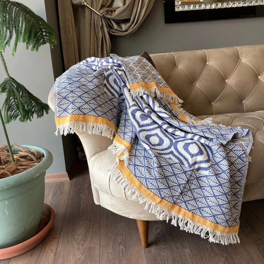 Trimita Asude plaid, blauw-wit geometrisch patroon met gele rand op een beige fauteuil