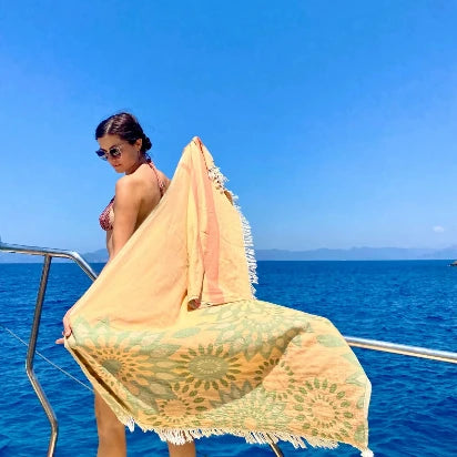 Woman using Trimita sunflower patterned orange peshtemal on a boat, showcasing a stylish and lightweight beach towel.