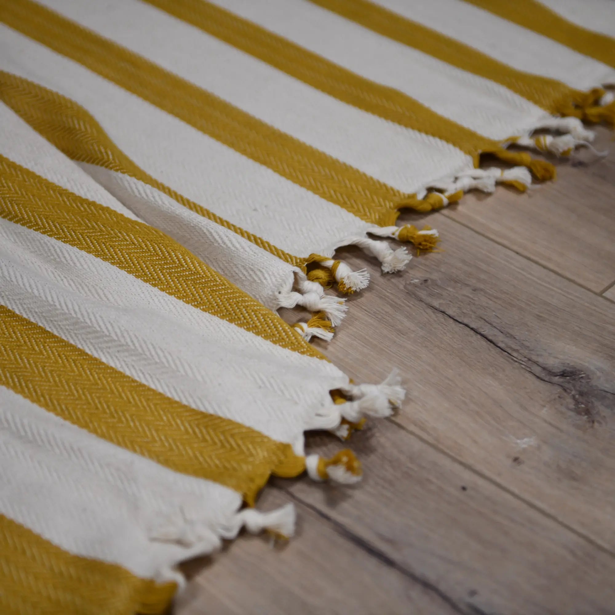 Yellow and white striped towel with tassels on a wooden floor