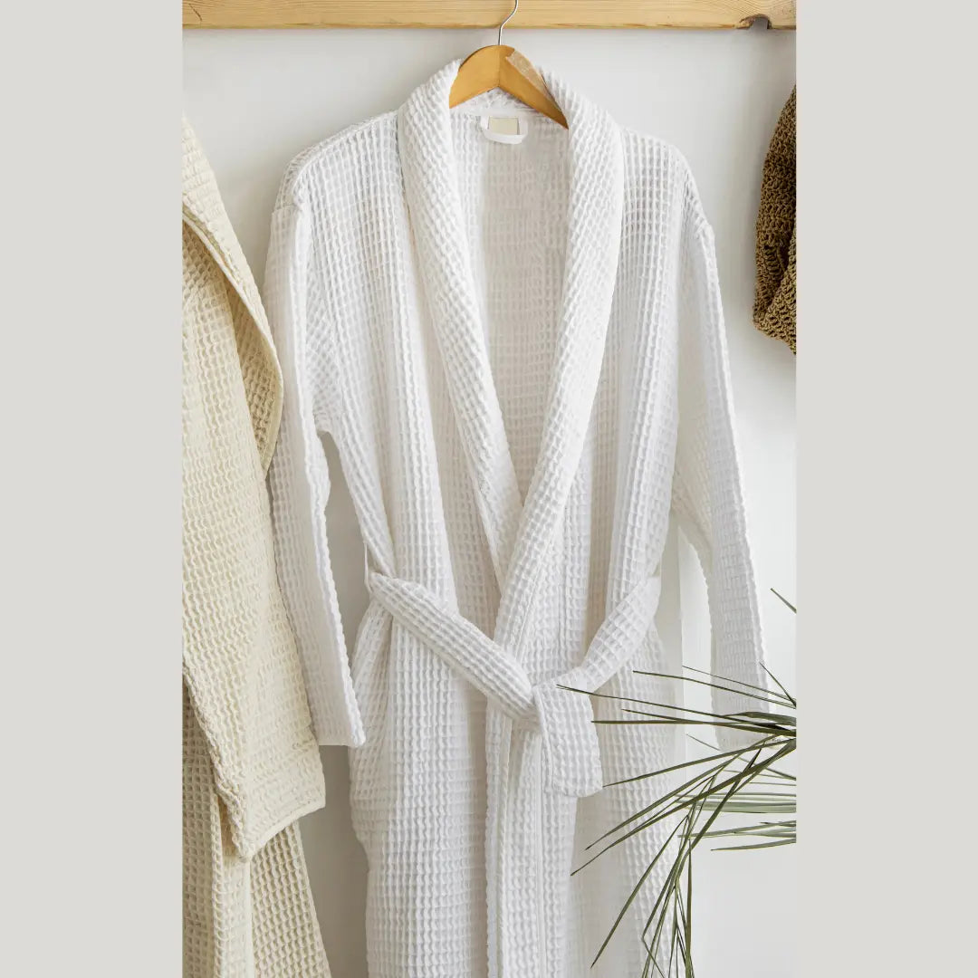 White textured Trimita 100% Turkish Cotton robe hanging on a wooden hanger against a white wall.