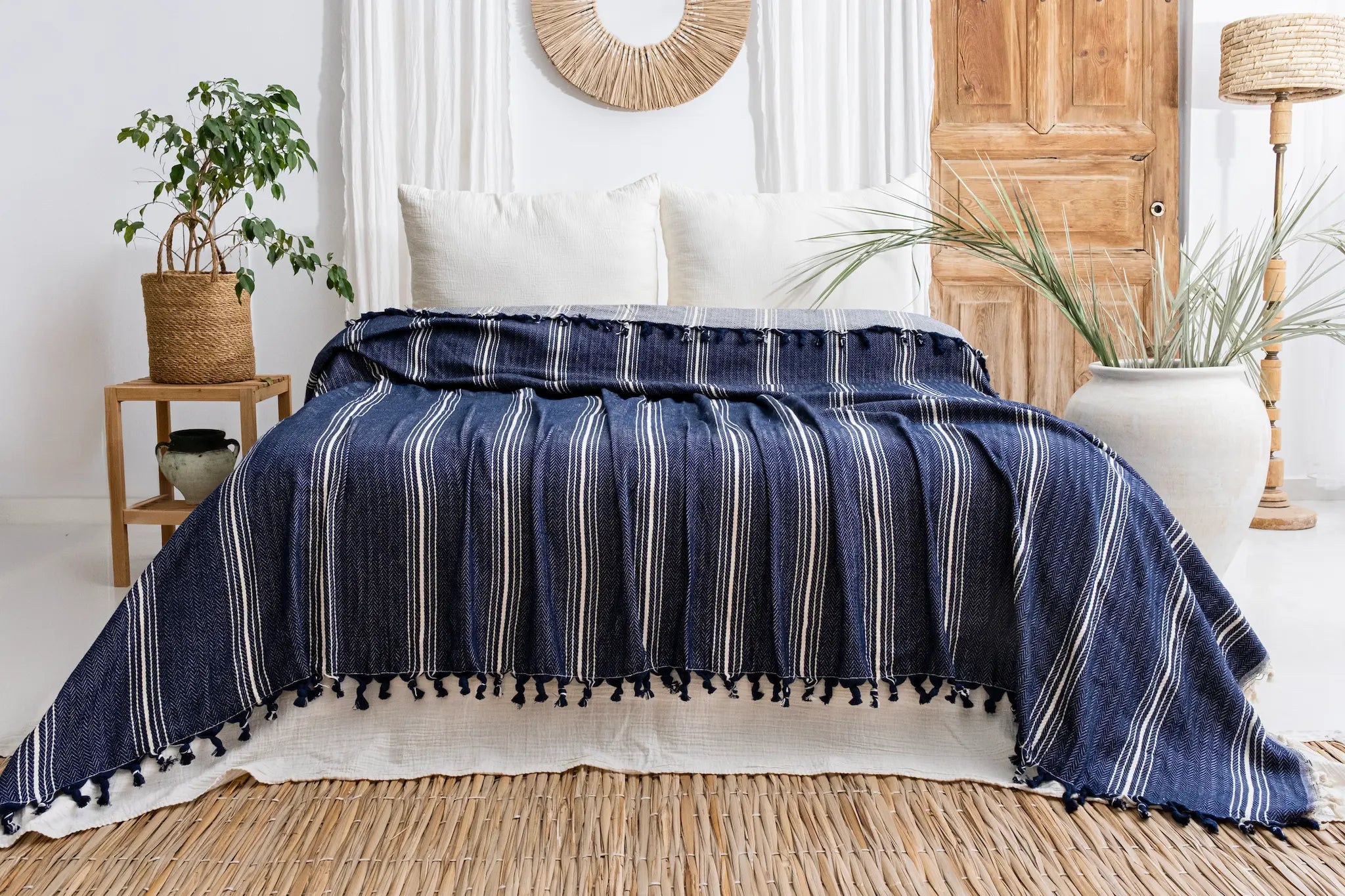 Navy blue striped blanket with tassels on a bed in a bedroom setting.