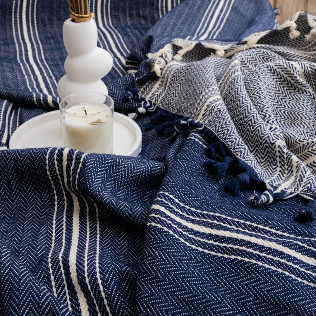 Close-up of a navy blue herringbone patterned cotton throw blanket with a white candle and minimalist vase.