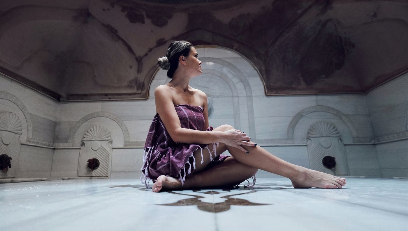 A girl wrapped in a Trimita towel sits in the middle of a Turkish bath.