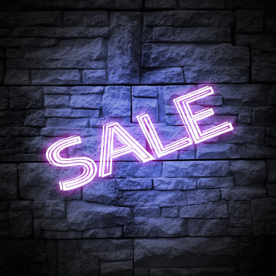 Enseigne au néon violet « SALE » sur un mur de briques foncées.