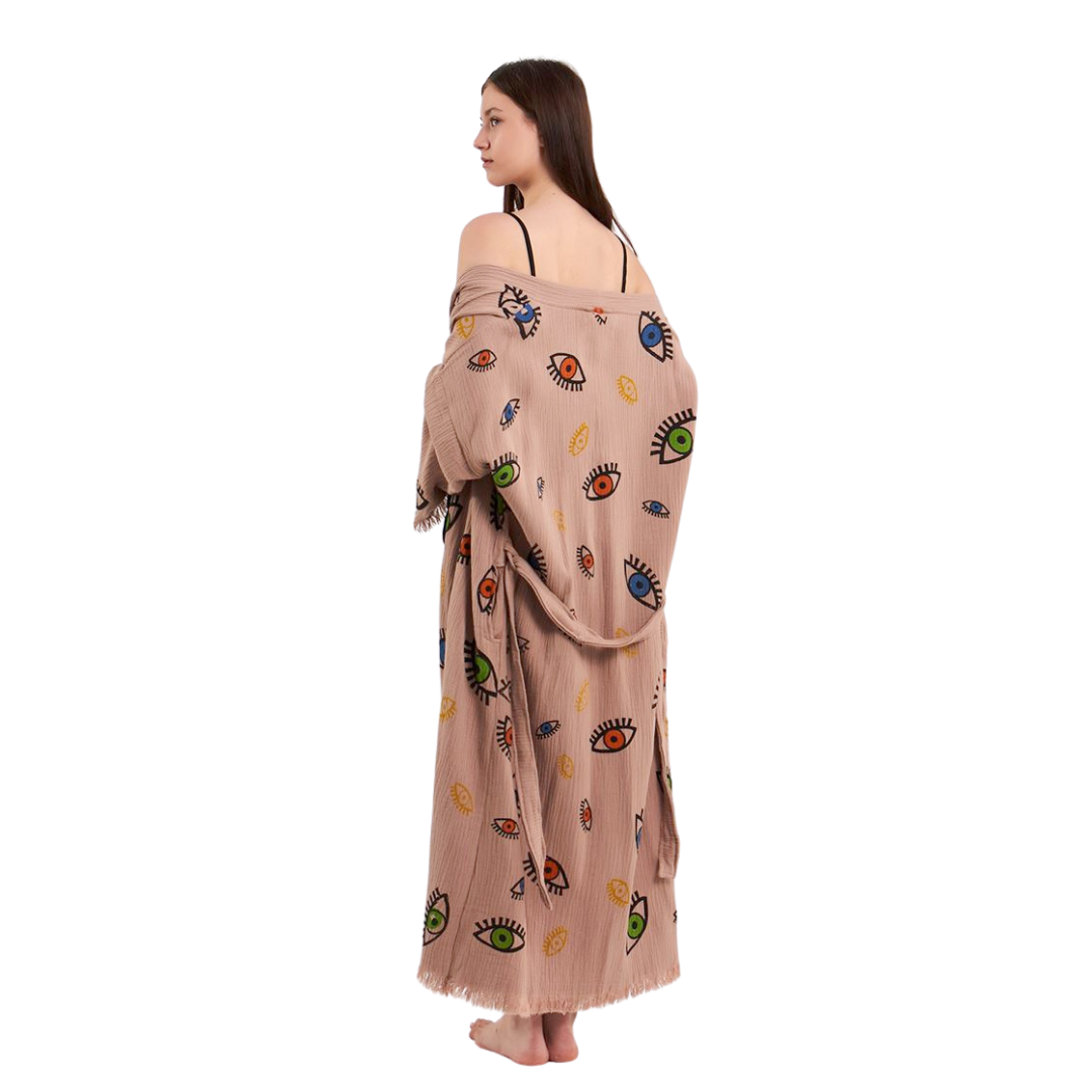 Model slightly turning, showing the back and side of a beige kimono robe with a colorful eye pattern, with the robe partially draped off the shoulder.