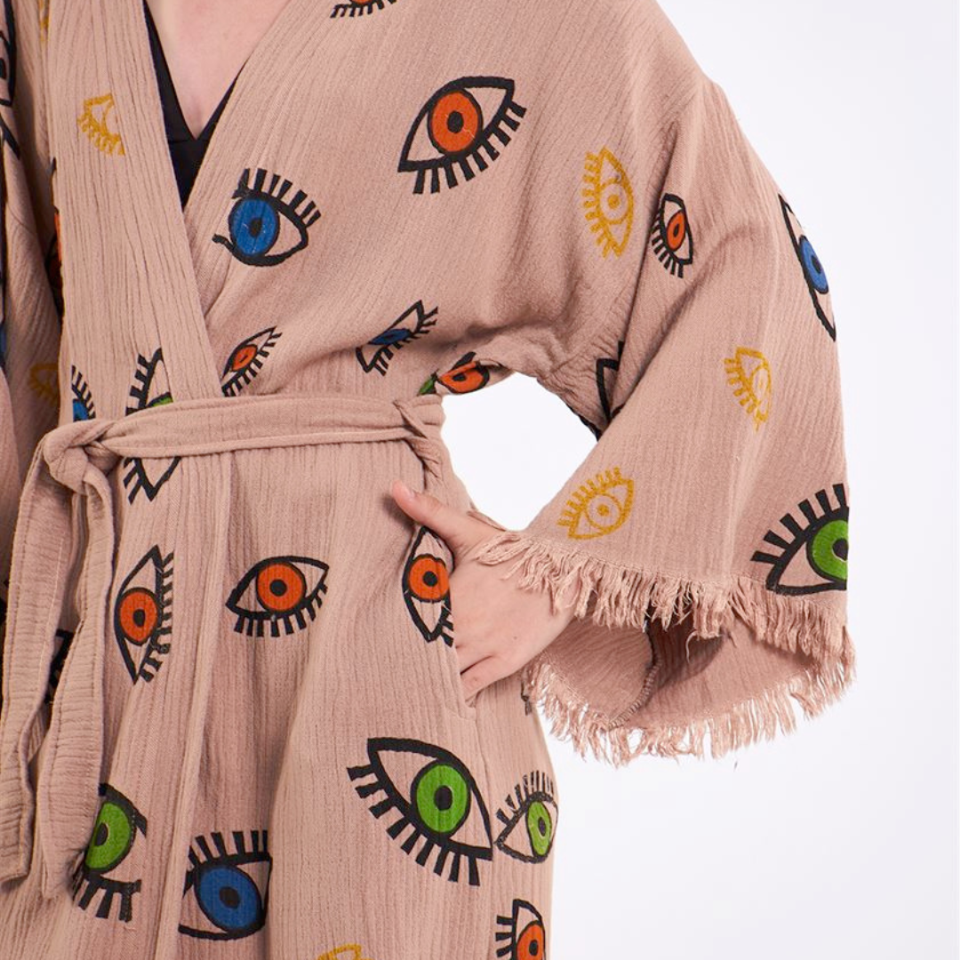 Close-up view of a beige kimono robe featuring a colorful eye pattern, with frayed edges on the sleeves.