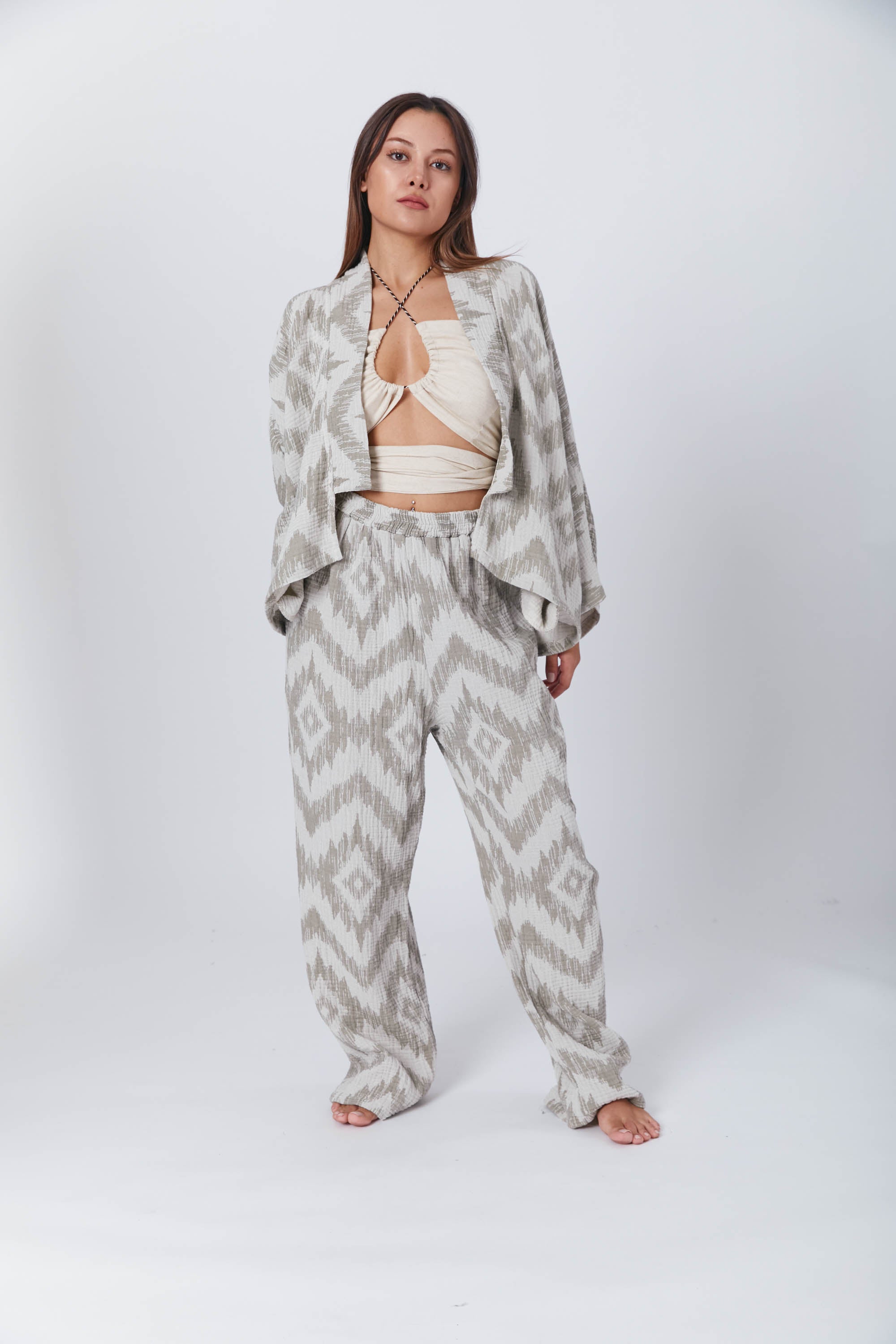 A woman posing in a coordinated loungewear set with a geometric pattern, consisting of loose pants and an open jacket over a cream halter crop top
