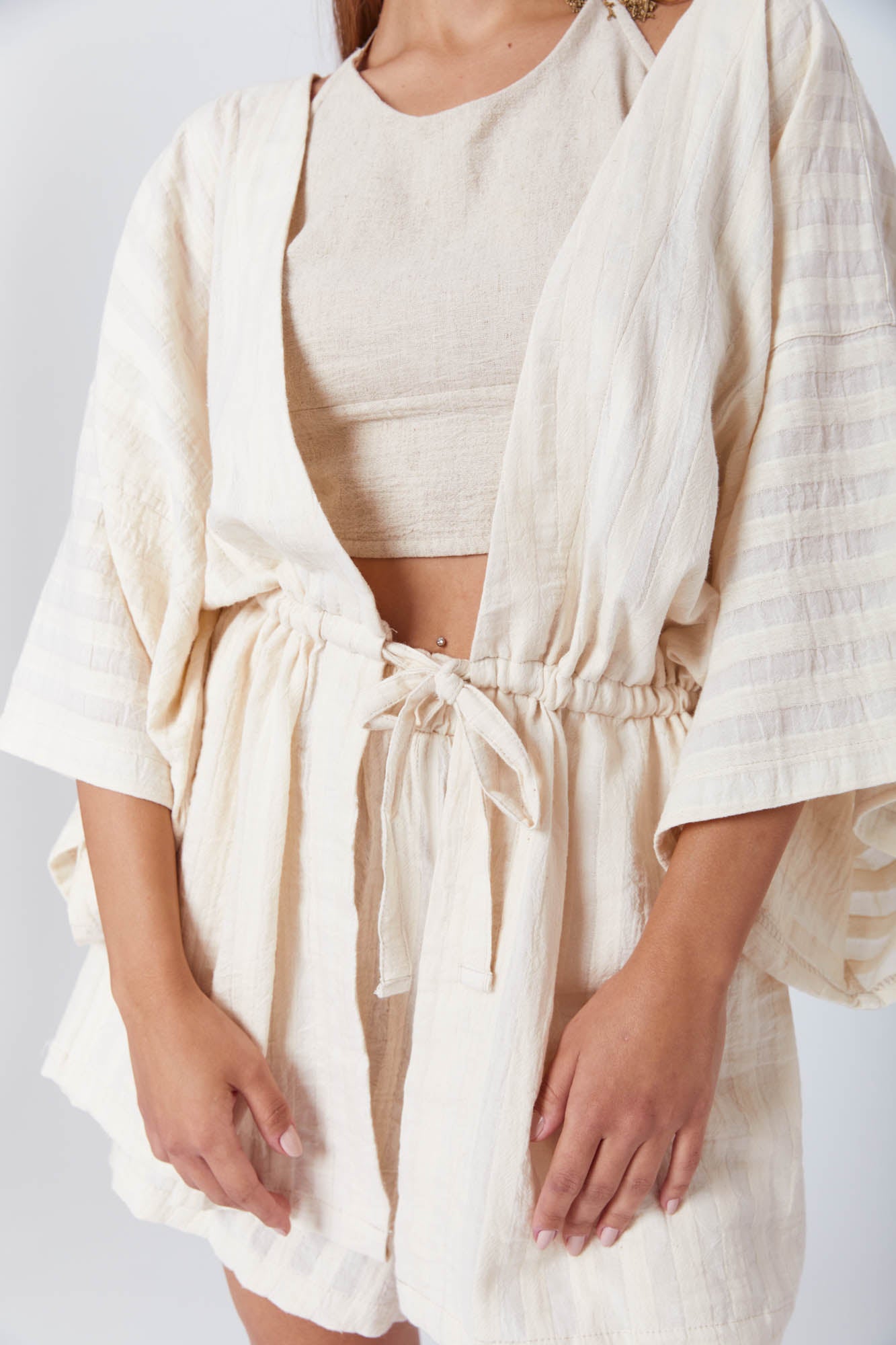 Young woman in minimalist, natural-toned clothing with a soft, flowing silhouette and subtle striped texture