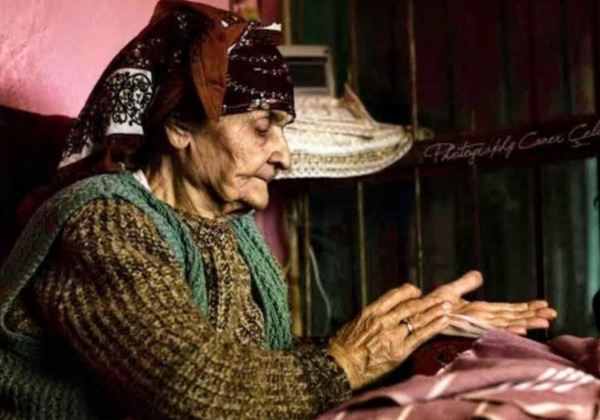 Een oudere vrouw knoopt met de hand de franjes van een roze hamamdoek.