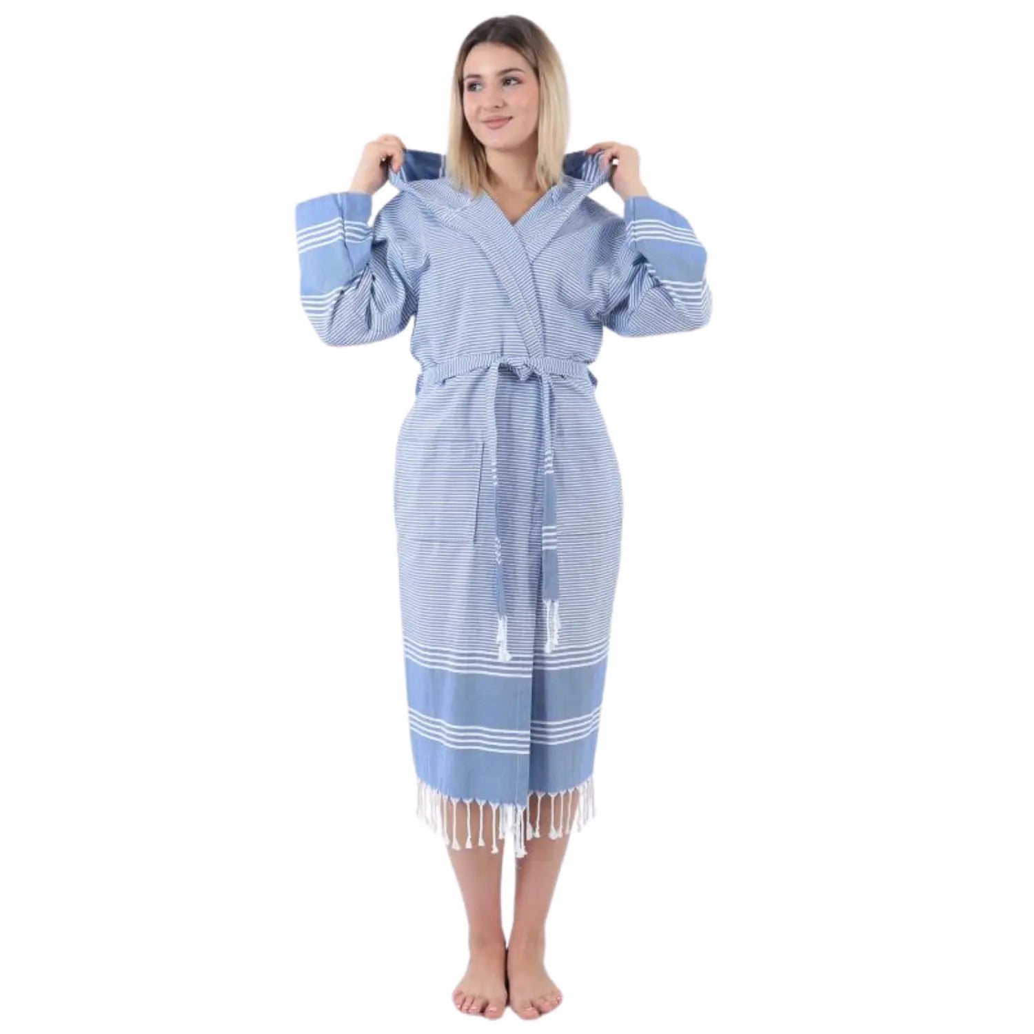 Front view of a woman wearing a light blue and white striped hooded Turkish cotton bathrobe with elegant tassels.