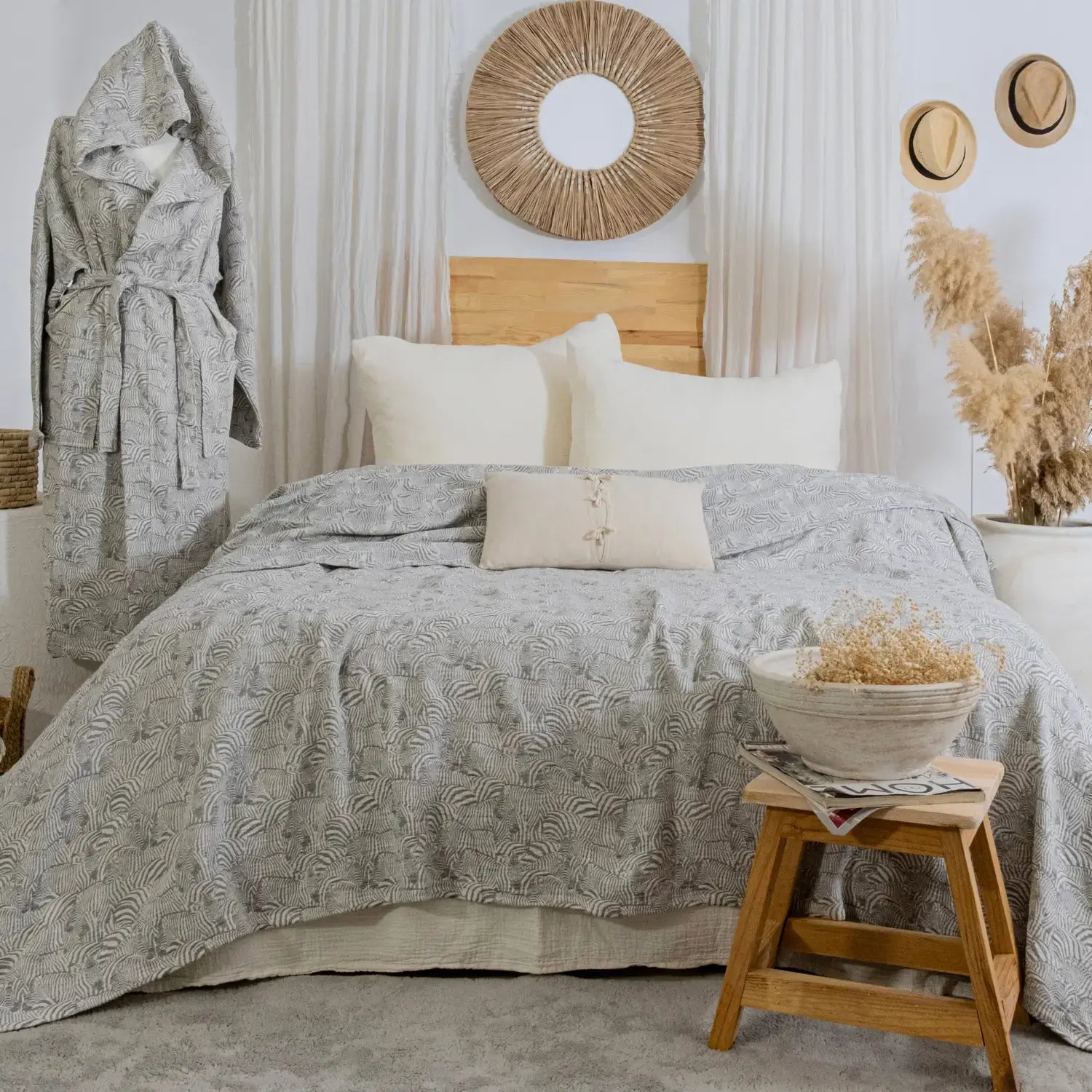 Boho-chic bedroom decor featuring a gray zebra patterned muslin bedspread on a bed with cream pillows and a wooden headboard.