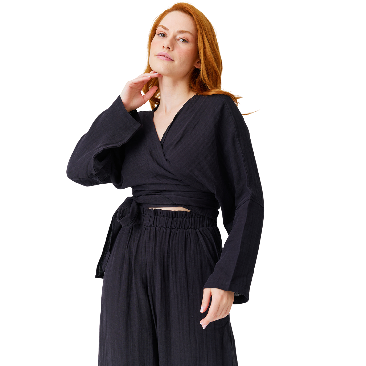 Studio portrait of a redheaded model looking at the camera, showcasing a minimalist black 100% cotton muslin wrap crop top with adjustable tie-waist.