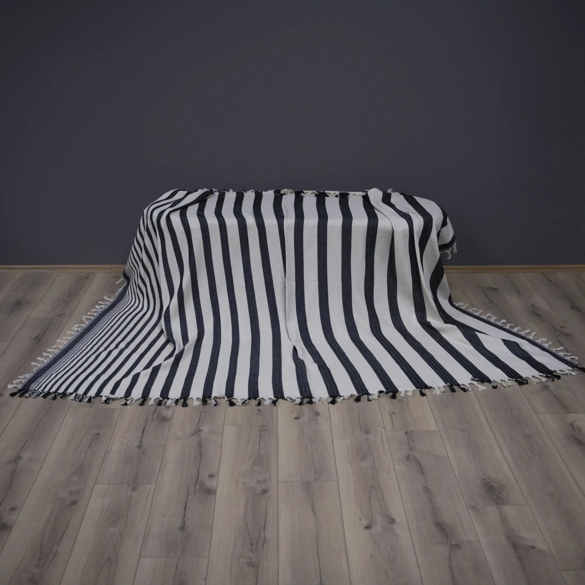 Timita Sevda Black and white striped blanket on a wooden floor with a dark gray wall background