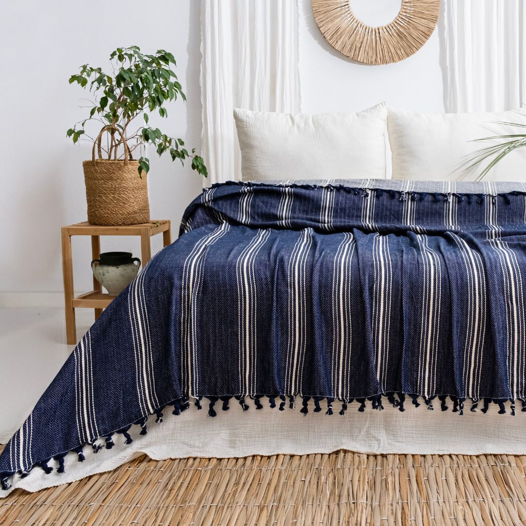 Yasmin Bedspread by Trimita – 100% natural cotton bedspread in navy with white stripes, styled on a bed with white pillows and a side table plant